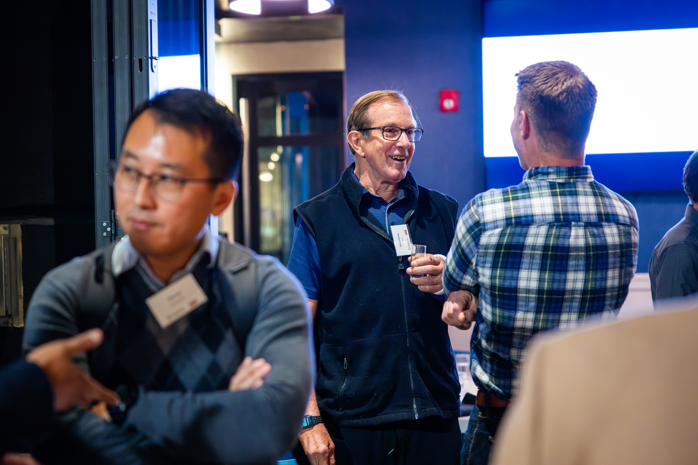 A senior executive laughing in mid-conversation with two colleagues at an evening event.