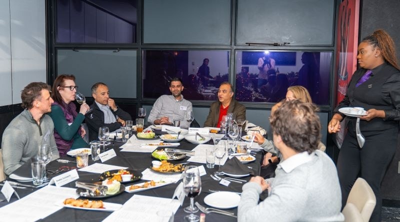 A server bringing plates to guests seated around a round dinner table.