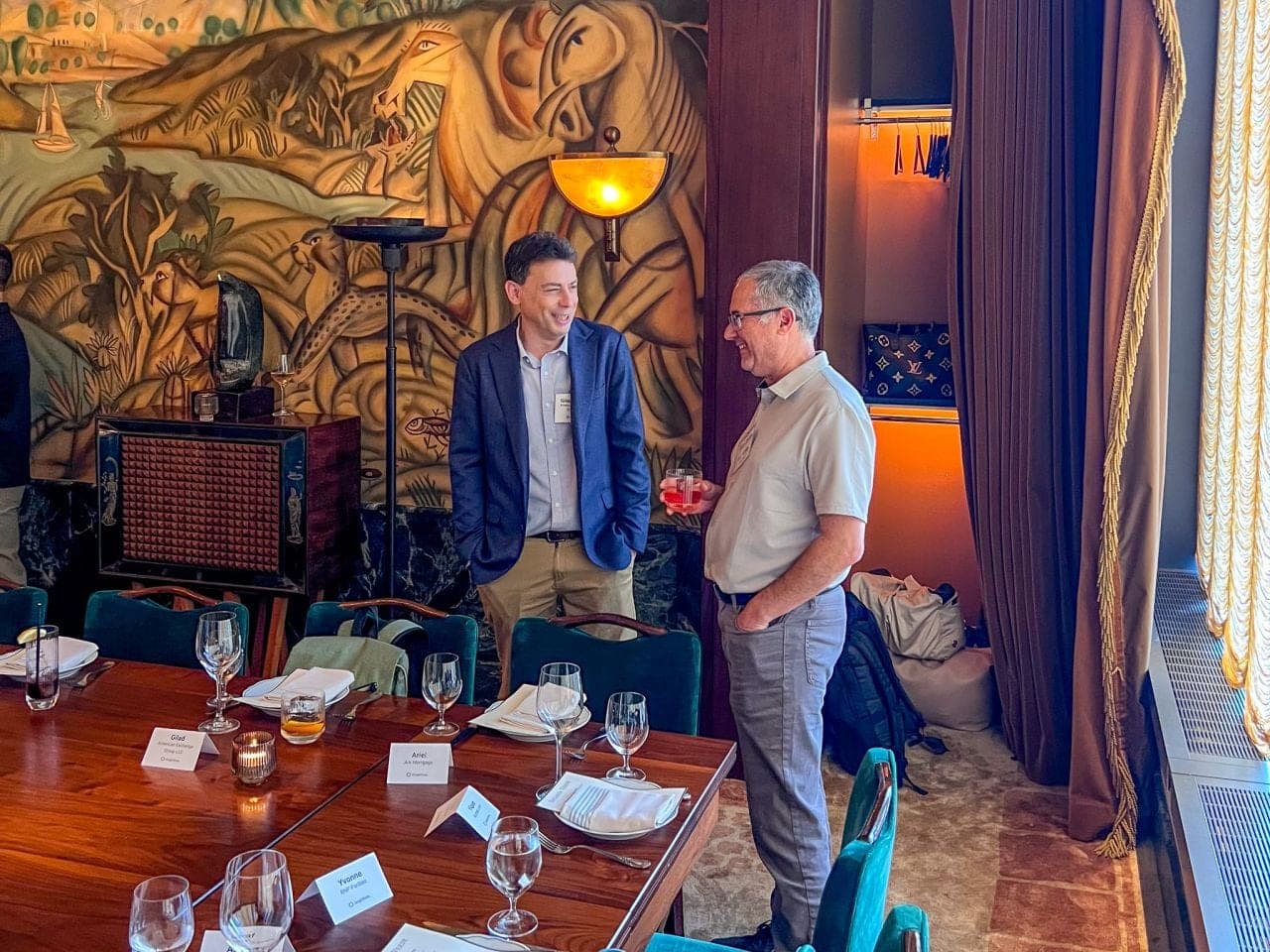 Two executives standing beside a set dinner table, mid-conversation and laughing.