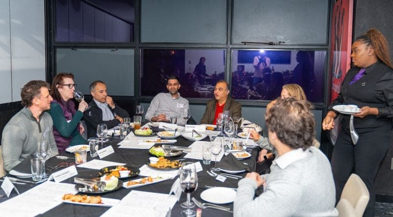 A server bringing plates to guests seated around a round dinner table.
